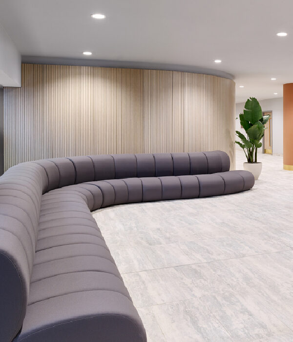 Banquette EPSILON en courbe taupe foncé installée le long d’un mur en bois dans un espace sanitaire de centre commercial
