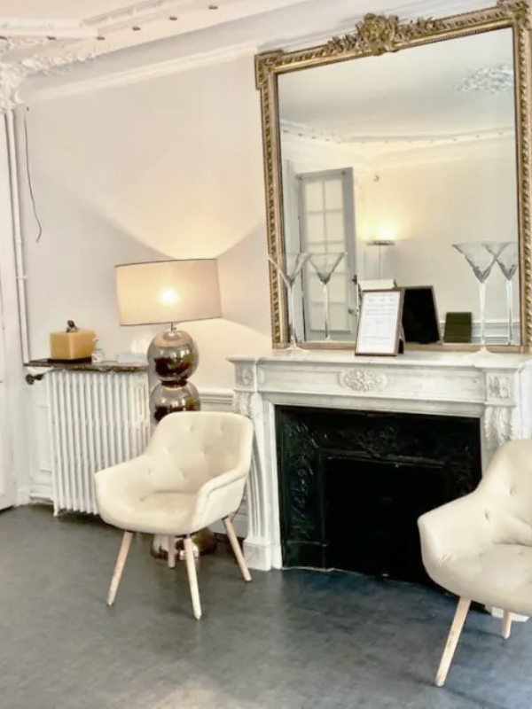 Deux fauteuils placés de chaque côté d’une cheminée dans une salle d’attente au style haussmannien parisien