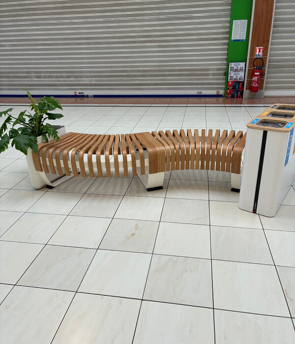 Banc bois GREENWOOD 4 places en forme S dans un centre commercial avec jardinière végétalisée et poubelle de recyclage en extrémité